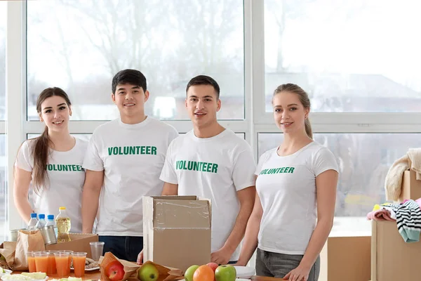 Young volunteers with food for poor people indoors — Stock Photo, Image