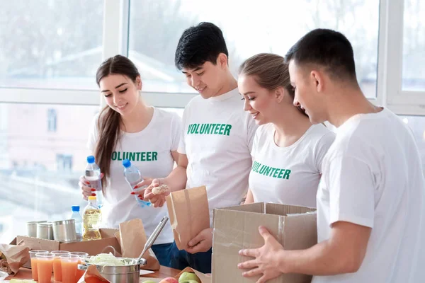 Young volunteers with food for poor people indoors — Stock Photo, Image