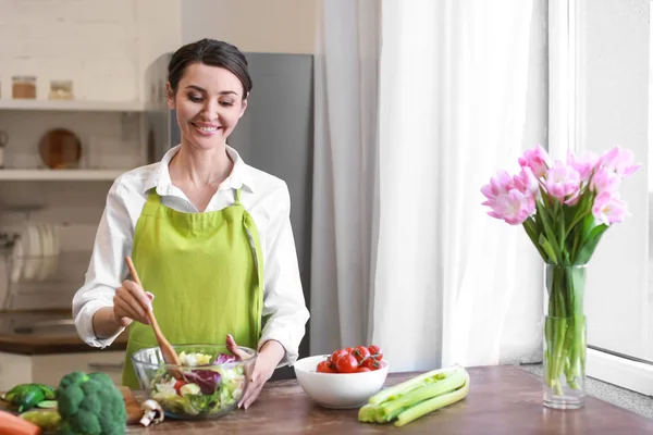 Beautiful woman preparing tasty vegetable salad in kitchen at home — Stock Photo, Image