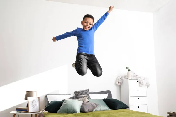 Happy African-American boy jumping on bed at home — Stock Photo, Image