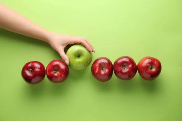 Weibliche Hand mit leckeren Äpfeln auf farbigem Hintergrund. Konzept der Einzigartigkeit — Stockfoto