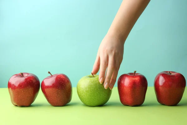 Weibliche Hand mit leckeren Äpfeln auf farbigem Hintergrund. Konzept der Einzigartigkeit — Stockfoto