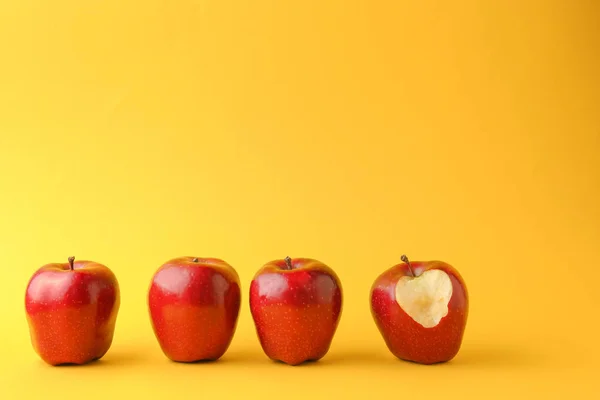 Bitten apple among whole ones on color background. Concept of uniqueness