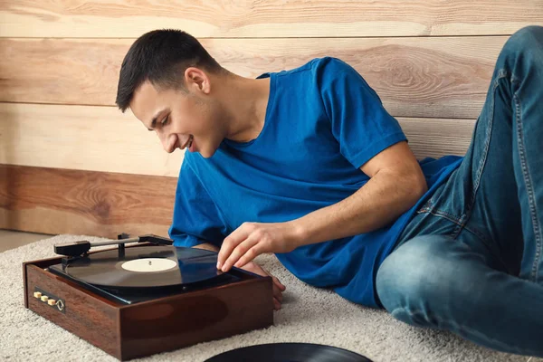 Young man listening to music on record player near wooden wall — Stock Photo, Image