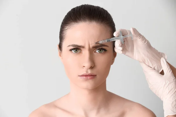 Mladá žena podáním injekce do obličeje na světlé pozadí — Stock fotografie