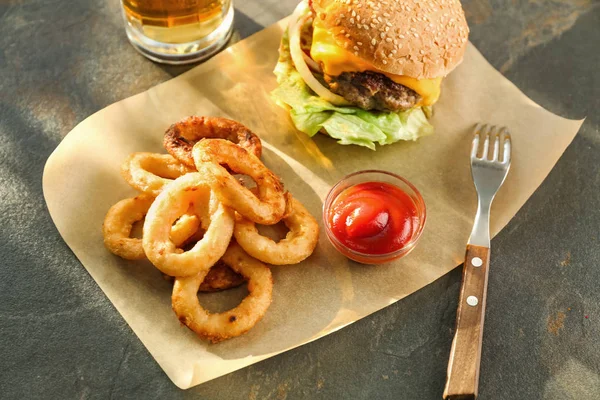 Tasty burger and onion rings on table — Stock Photo, Image