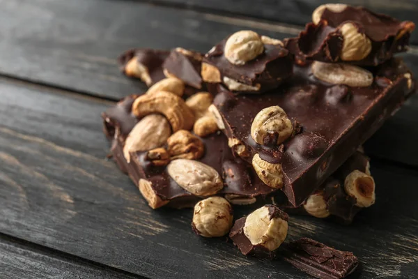 Pieces of tasty dark chocolate with nuts on wooden background — Stock Photo, Image