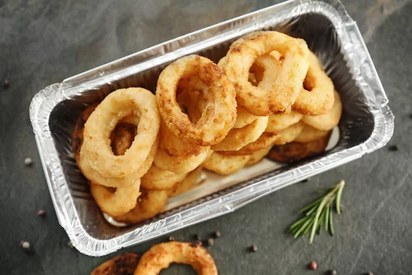 Takeaway box with tasty onion rings on grey table — Stock Photo, Image