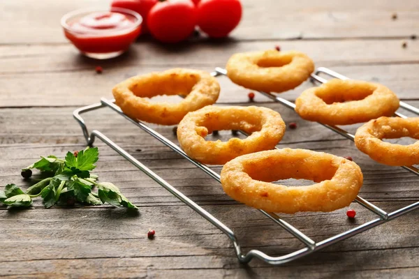 Cooling rack with tasty onion rings on wooden table — Stock Photo, Image
