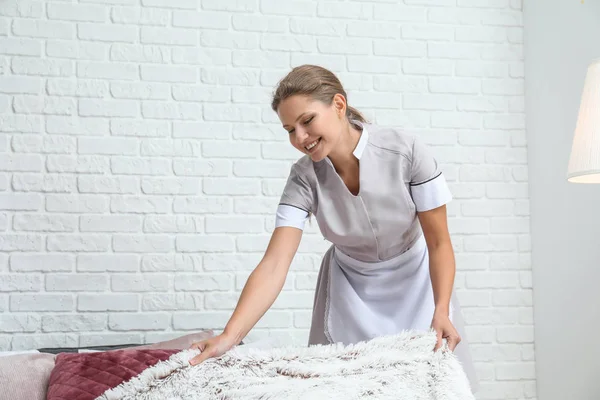 Beautiful female housekeeper making bed in room — Stock Photo, Image
