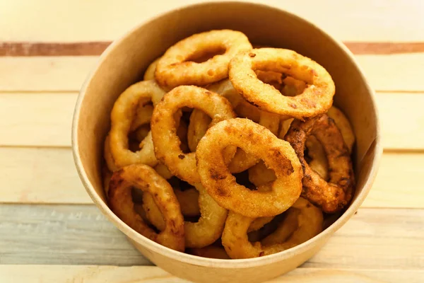 Cardboard bowl with tasty onion rings on wooden table — Stock Photo, Image