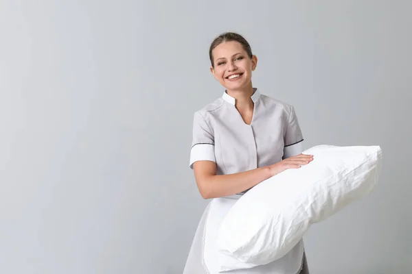 Beautiful female housekeeper with soft pillow on grey background — Stock Photo, Image