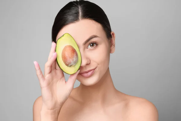 Portrait of beautiful woman with avocado on grey background — Stock Photo, Image