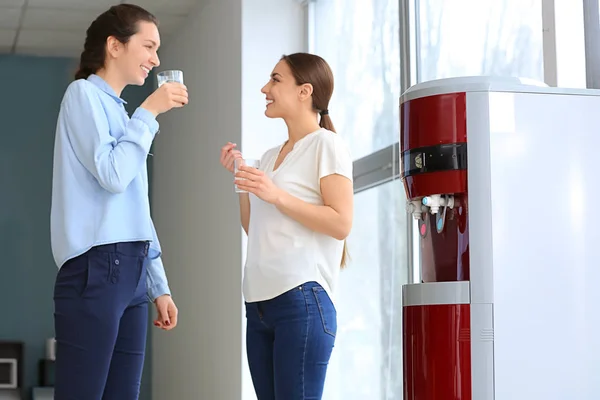 Colleagues drinking water from cooler during break in office