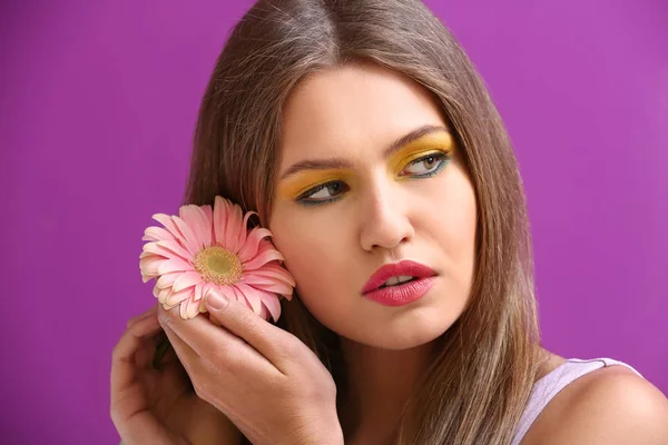 Beautiful young woman with bright makeup and flower on color background — Stock Photo, Image