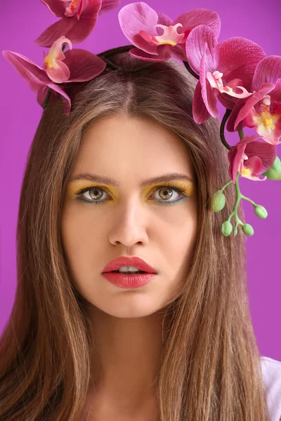 Красивая молодая женщина с ярким макияжем и цветами на фоне цвета — стоковое фото