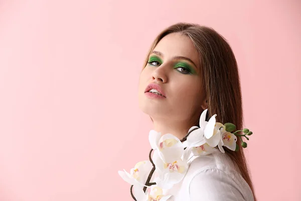 Bella giovane donna con trucco luminoso e fiori su sfondo di colore — Foto Stock