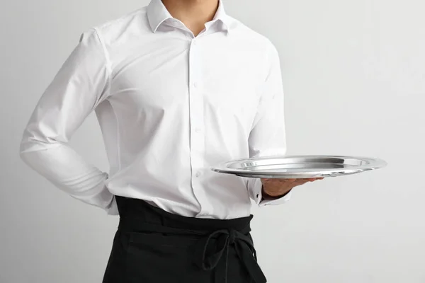 Knappe kelner met lege lade op lichte achtergrond — Stockfoto