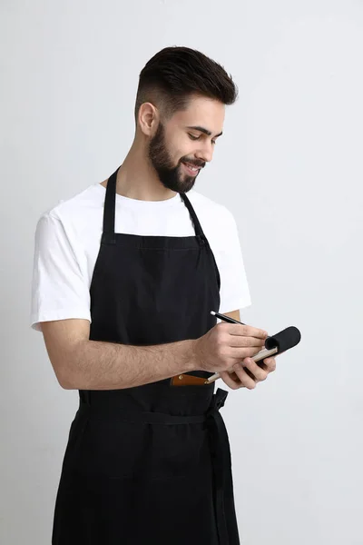 Przystojny kelner z notebooka na jasnym tle — Zdjęcie stockowe