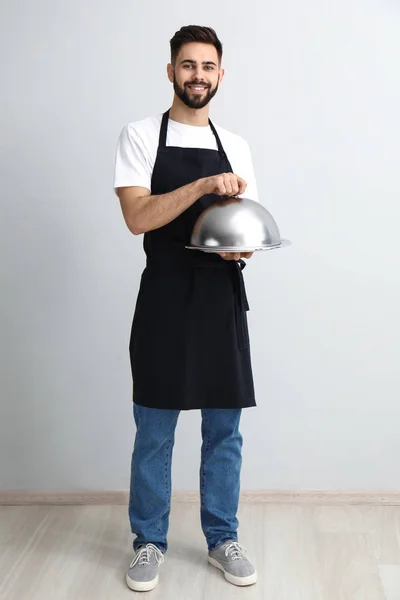 Garçom bonito com bandeja e cloche perto da parede de luz — Fotografia de Stock