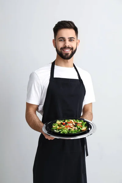 Handsome waiter with fresh salad on light background — Stock Photo, Image