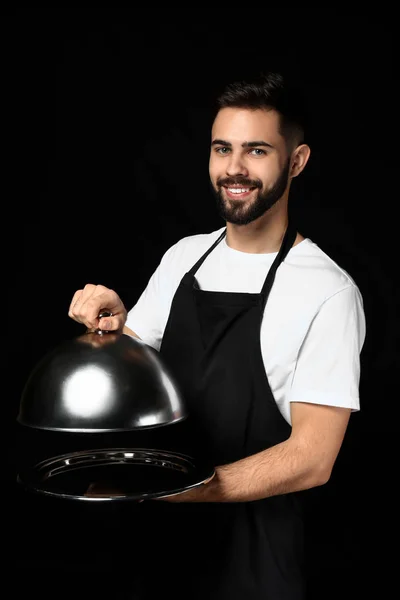 Handsome waiter with tray and cloche on dark background — Stock Photo, Image