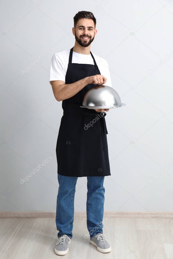 Handsome waiter with tray and cloche near light wall