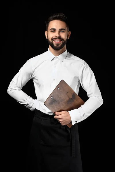 Handsome waiter with menu on dark background — Stock Photo, Image