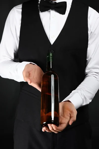 Handsome waiter with bottle of wine on dark background