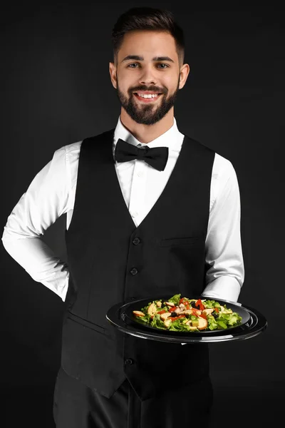 Handsome waiter with fresh salad on dark background — Stock Photo, Image
