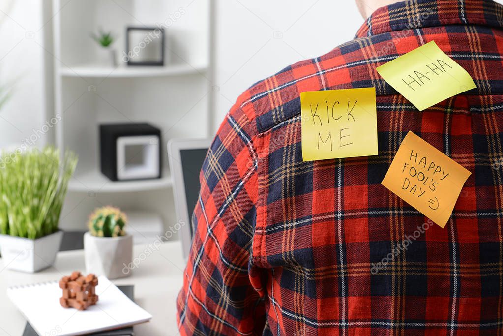 Sticky notes on back of young man working in office. April Fool's Day prank