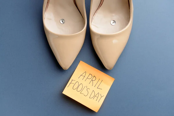 Vrouwelijke schoenen met pinnen en kleverige nota met tekst April Fool'S Day op kleur achtergrond — Stockfoto