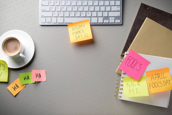 Computer keyboard with cup of coffee and sticky notes on grey background. April Fool's Day prank Royalty Free Stock Photos