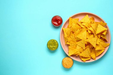 Renkli arkaplanda lezzetli nachos ve soslu tabak.