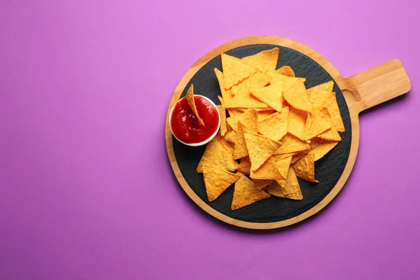 Board with tasty nachos and sauce on color background — Stock Photo, Image