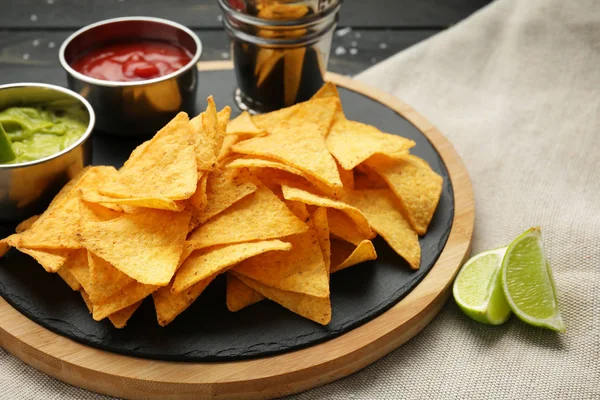 Placa com nachos saborosos e molhos na mesa — Fotografia de Stock