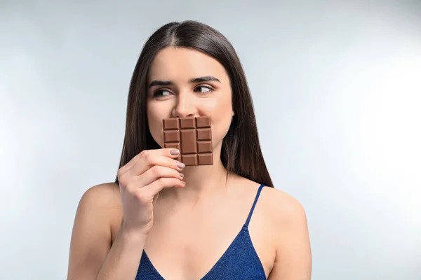 Beautiful young woman with tasty chocolate on light background — Stock Photo, Image