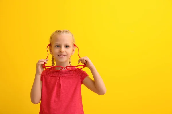 Забавная маленькая девочка с большими очками в форме сердца на цветном фоне. Празднование Дня дураков — стоковое фото