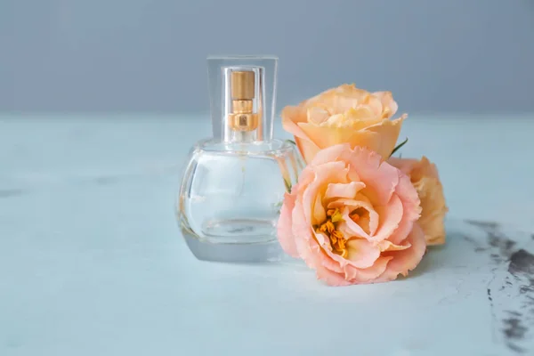 Transparent bottle of perfume with beautiful flowers on light table — Stock Photo, Image