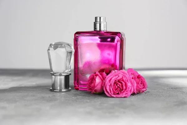 Frasco transparente de perfume com belas flores na mesa cinza — Fotografia de Stock