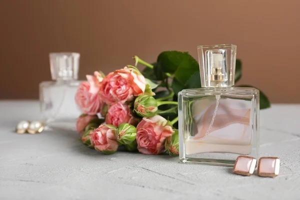 Průhledné lahvičky s parfémy s krásnými květinami a náušnice na šedý stůl — Stock fotografie