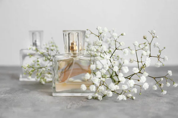 Frasco transparente de perfume con hermosas flores sobre mesa gris —  Fotos de Stock