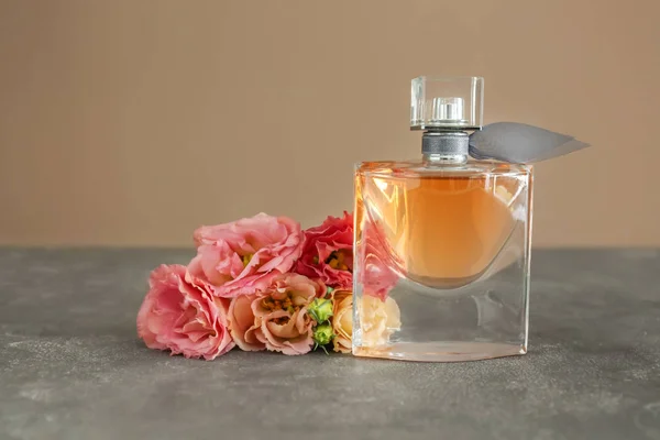 Frasco transparente de perfume com belas flores na mesa cinza — Fotografia de Stock
