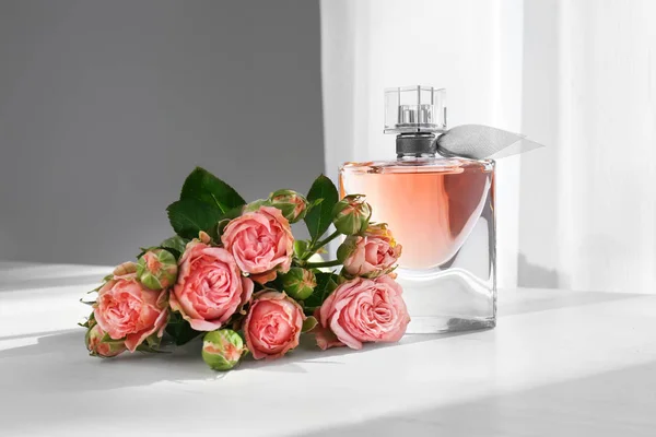 Frasco transparente de perfume com belas flores na mesa branca — Fotografia de Stock