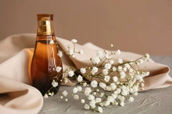 Doorzichtige fles parfum met prachtige bloemen op grijze tafel — Stockfoto