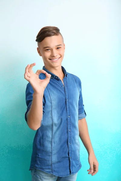 Smiling teenage boy showing OK gesture on color background — Stock Photo, Image