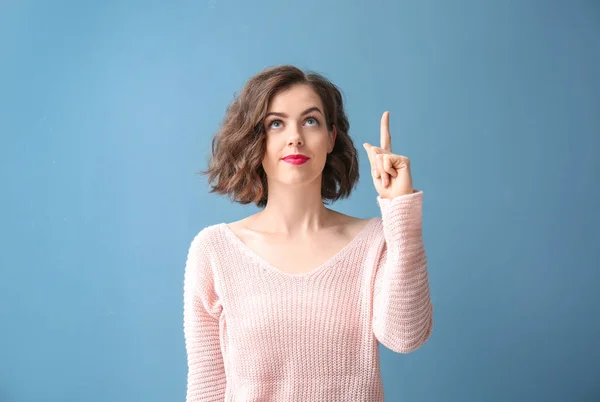 Portrait of beautiful woman with raised index finger on color background — Stock Photo, Image