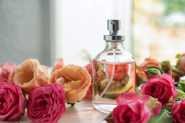 Бутылка духов с красивыми цветами на белом столе — стоковое фото