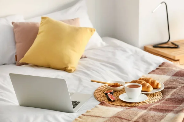Wicker mat with delicious breakfast and laptop on bed
