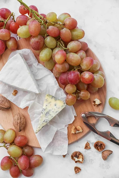 Érett lédús szőlő, sajt és dió fából készült táblán — Stock Fotó
